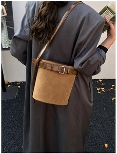 Détail du sac seau en daim marron avec sangle en cuir sur fond de feuilles de ginkgo