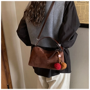 Detail view of brown suede underarm bag with decorative plush pom-pom charms