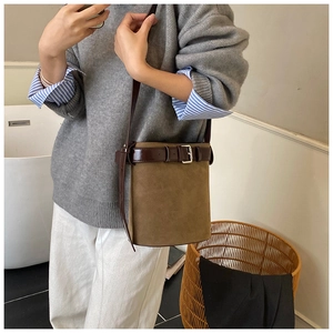 Detailed view of brown matte leather bucket bag with buckle strap on a model shoulder