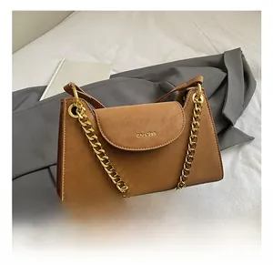 Détail d'un sac à rabat en cuir mat marron avec chaîne dorée sur fond de blazer gris