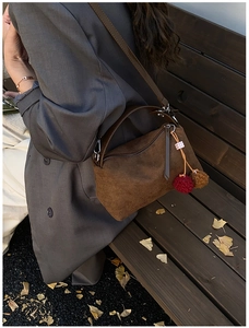 Detail of a brown suede crossbody bag with leather handles and a fuzzy pompom charm