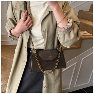 Detail of dark brown matte leather bag with chunky gold chain strap and branding