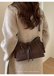 Detail der dunkelbraunen Wildleder-Schultertasche mit Kontrastnähten und Logo-Anhänger