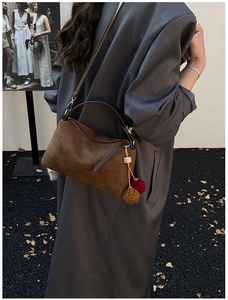 Sac Boston en daim marron avec breloque, porté par un mannequin en blazer gris chic