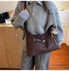 Close-up of a large dark brown suede tote bag with leather straps and a plush puppy charm