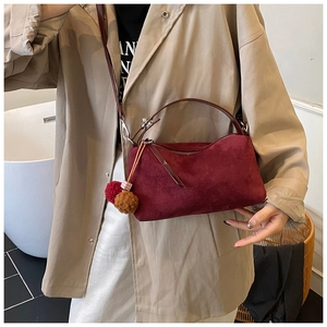 Close-up of burgundy suede handbag with elegant pompom charm and silver hardware detail