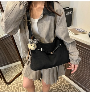Detail of black dumpling shoulder bag with metal buckle and cute bear charm accessory