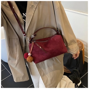 Burgundy suede pillow bag with plush pom-pom charm shown worn crossbody by a model