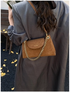 Close-up of a brown textured shoulder bag with gold chain strap on a wooden bench