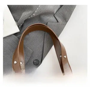 Close-up of brown leather bag handle featuring decorative silver metal rivets and studs