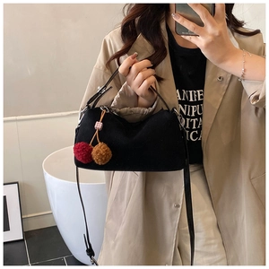 Detail of black suede underarm bag featuring decorative plush ball charm for winter