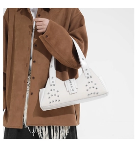 Close-up of white punk-style shoulder bag with silver rivets and wide strap on model
