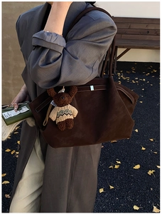 Détail d'un sac cabas en daim marron avec pendentif ours sur fond de feuilles d'automne