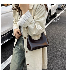 Detail of dark brown glossy hobo bag in half-moon shape with minimalist leather texture