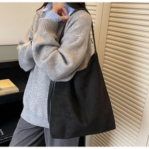 Side view of large black faux suede tote bag on shoulder with casual outfit