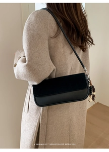 Detail of black baguette bag with suede flap and wooden bead charm on beige coat