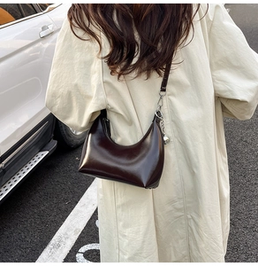 Détail du sac Hobo en cuir brillant marron foncé avec pendentif boule argentée sur la bandoulière