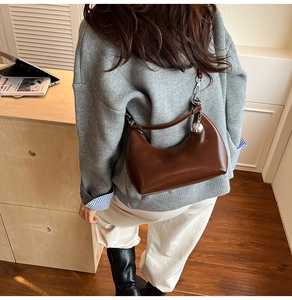 Close-up of brown semi-circular leather bag with silver metal ball accent and zipper