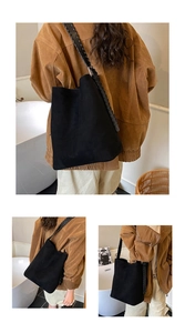 Close-up of black faux suede bucket bag featuring a wide woven shoulder strap and hobo style