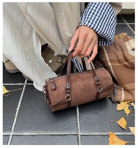 Close-up of brown suede bowling bag with leather trim and gold zipper in autumn setting