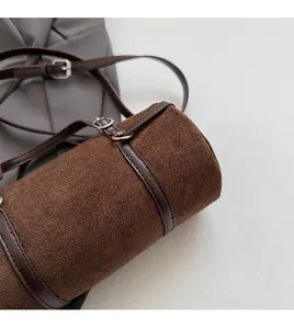Detailed macro view of brown suede cylinder bag featuring fine stitching and silver metal buckle