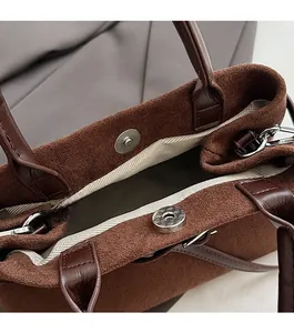 Detail of magnetic snap closure and suede texture on a brown bucket bag with lining