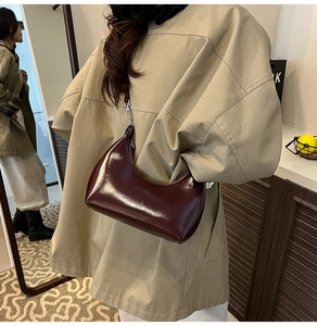 Detail view of glossy burgundy leather underarm bag with curved lines and metal hardware