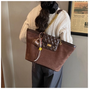 Detail of a brown suede tote bag with quilted front pocket and gold chain strap accent