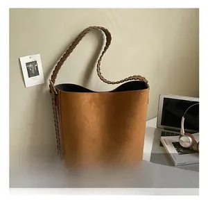 Detail of a brown suede bucket bag featuring a wide woven leather shoulder strap