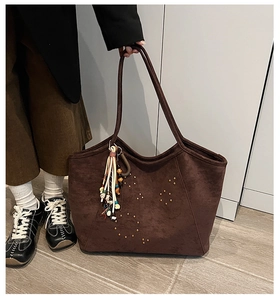 Detail of dark brown suede tote bag with golden rivets and a colorful tassel charm
