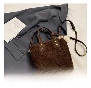 Close-up of deep brown plush bucket bag with fuzzy pompom charm and leather strap details