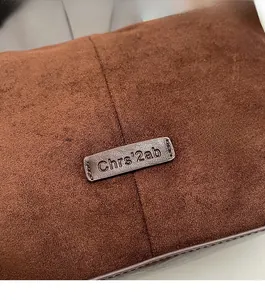 Detail of metal brand plaque and stitched seam on brown suede crossbody bag
