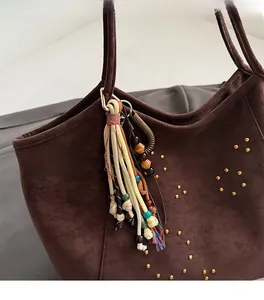 Detail of bohemian tassel charm with wooden beads on a brown suede tote bag