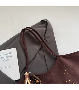 Detail view of brown suede tote bag featuring metallic rivets and a colorful tassel pendant