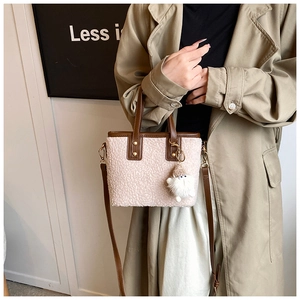 Detail of plush beige bucket bag with brown leather handles and cute plush doll charm
