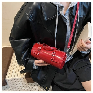 Detail showing red glossy cylindrical crossbody bag with silver buckles and red strap