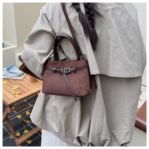 Detail einer dunkelbraunen Wildlederhandtasche mit Metallschnalle und langem Schultergurt