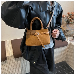 Detailed view of brown suede handbag with decorative buckle and dual carry handles