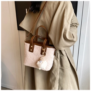 Détail du sac seau en peluche avec bordure en cuir marron, rivets et breloque blanche