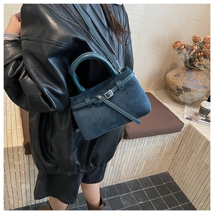 Detailed view of dark teal matte suede bucket bag with retro buckle and stone steps backdrop