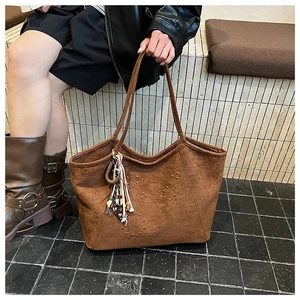 Detail der braunen Wildleder-Tragetasche mit Nieten und Boho-Quasten-Anhänger