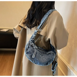 Detail view of a vintage denim crescent bag with a matching mini pouch on a trench coat