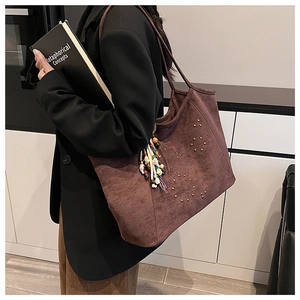 Détail d'un sac cabas en daim marron foncé avec rivets dorés et glands en perles