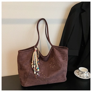 Detail of dark brown suede tote bag featuring gold star studs and a colorful fringe tassel