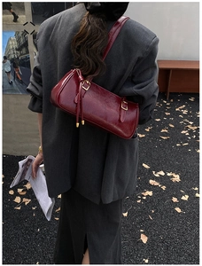 Détail d'un sac d'épaule en cuir verni rouge foncé avec boucle dorée sur blazer gris