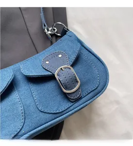 Detail of blue denim shoulder bag with silver metal buckle and contrast stitching