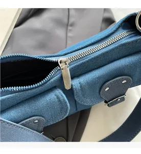 Detailed close-up of smooth silver metal zipper and rivet design on denim shoulder bag