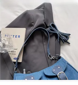 Detail of blue denim shoulder bag with silver rivets and dual straps on grey blazer