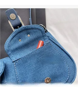 Detail of blue denim saddle bag featuring inner pocket with lipstick for size scale