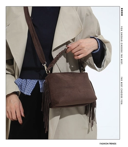 Detail of dark brown suede bag with long fringes, woven handle and wide canvas strap